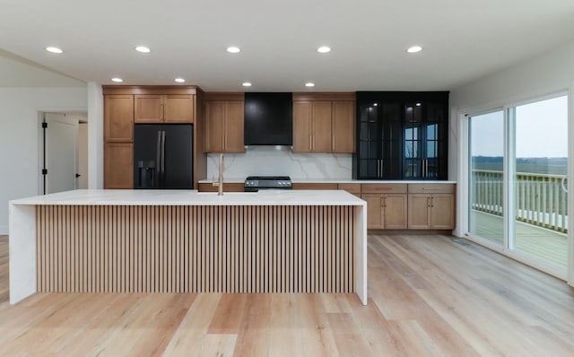 kitchen featuring backsplash, stove, black refrigerator with ice dispenser, range hood, and light countertops