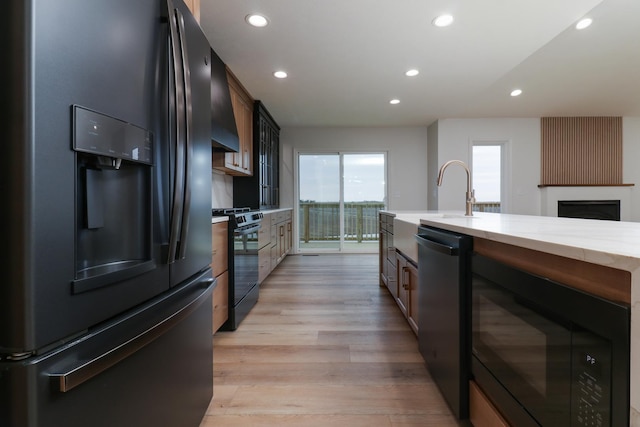 kitchen with black appliances, light wood-style flooring, a fireplace, light stone countertops, and recessed lighting
