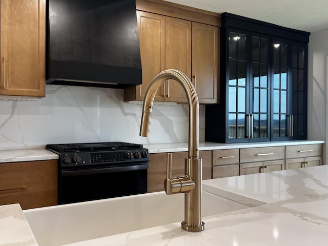details with backsplash, brown cabinetry, black gas range, and range hood