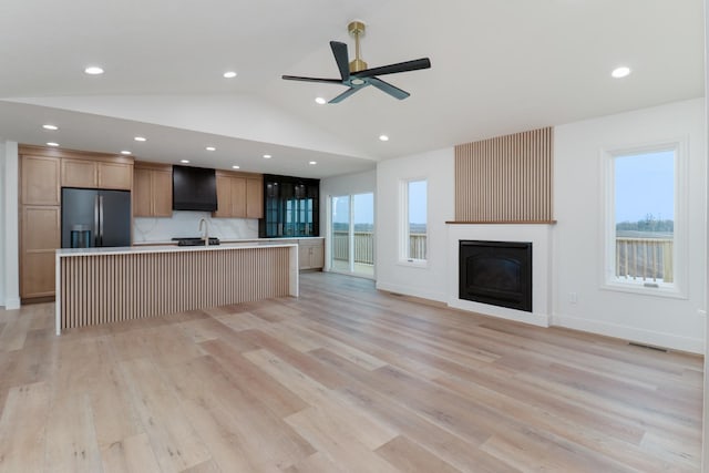 unfurnished living room featuring visible vents, a ceiling fan, a sink, a glass covered fireplace, and light wood-style flooring