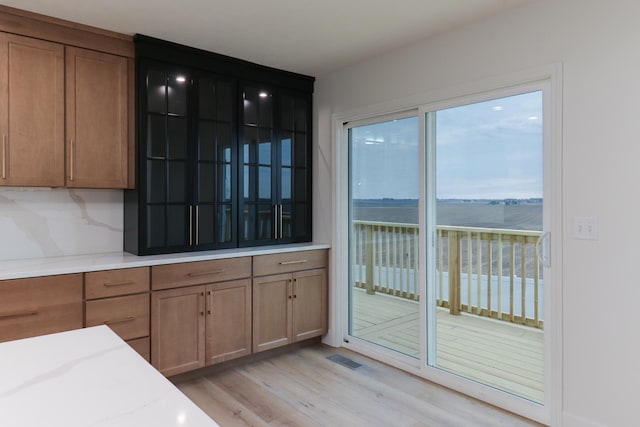 kitchen with light wood finished floors, visible vents, glass insert cabinets, light stone countertops, and brown cabinetry