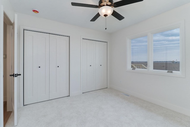 unfurnished bedroom with multiple closets, visible vents, baseboards, carpet flooring, and ceiling fan