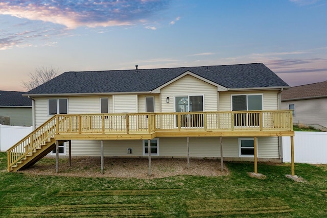 back of property at dusk with a lawn, roof with shingles, and stairs