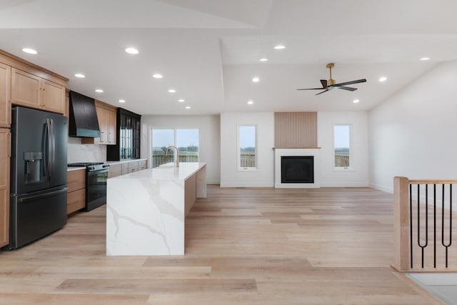 kitchen featuring black appliances, wall chimney exhaust hood, light stone counters, and light wood-style floors
