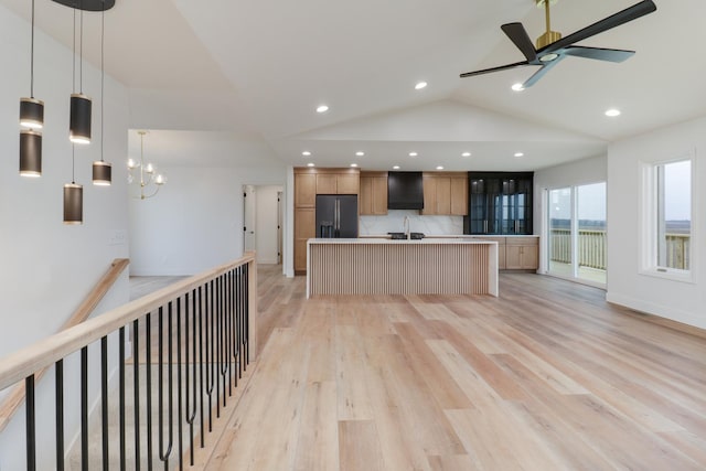 kitchen featuring light wood finished floors, a sink, ceiling fan with notable chandelier, black refrigerator with ice dispenser, and wall chimney range hood