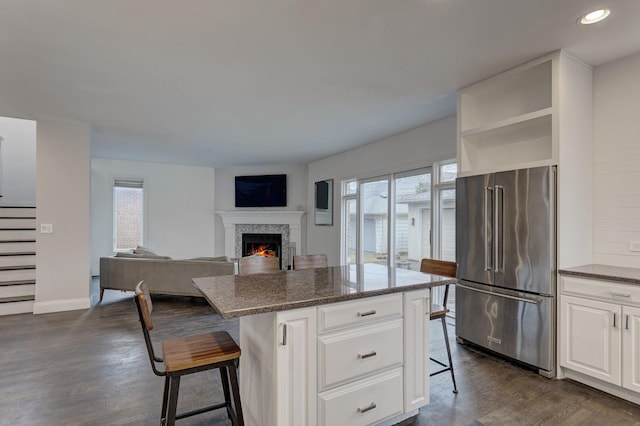 kitchen with white cabinetry, a center island, high quality fridge, a kitchen breakfast bar, and dark stone counters