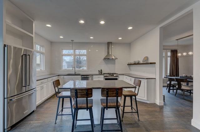 kitchen featuring appliances with stainless steel finishes, sink, white cabinets, a center island, and wall chimney exhaust hood