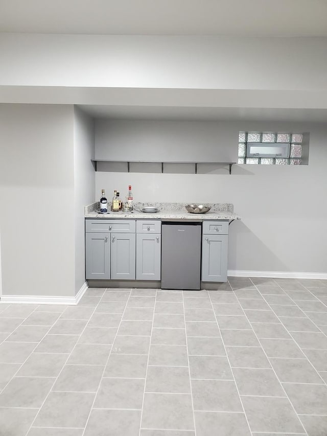 kitchen featuring light tile patterned flooring, stainless steel fridge, light stone countertops, and gray cabinetry