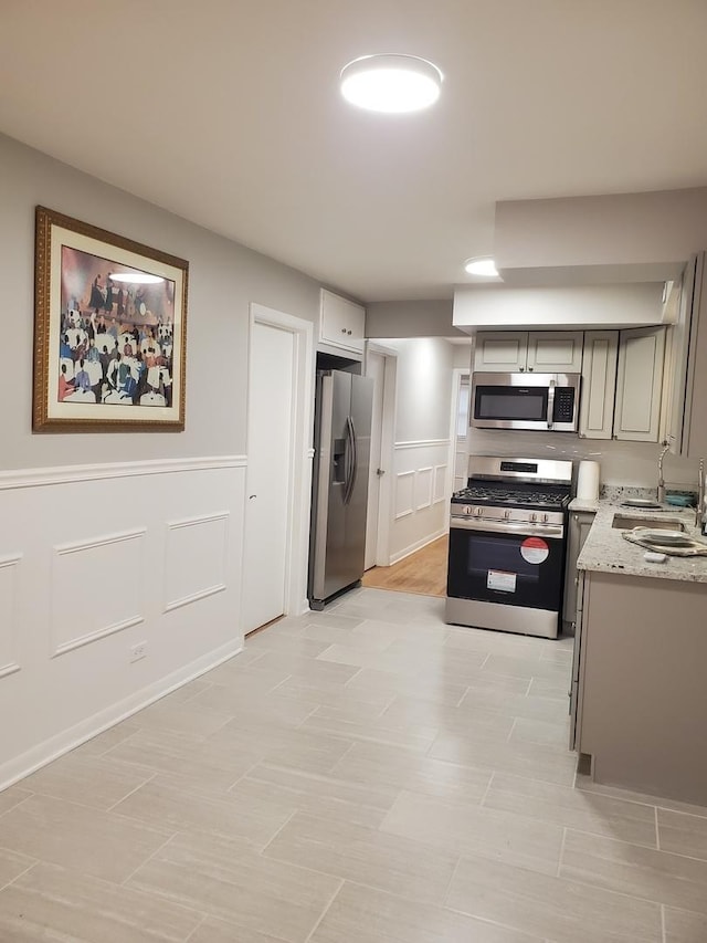 kitchen featuring light stone counters, appliances with stainless steel finishes, sink, and gray cabinetry