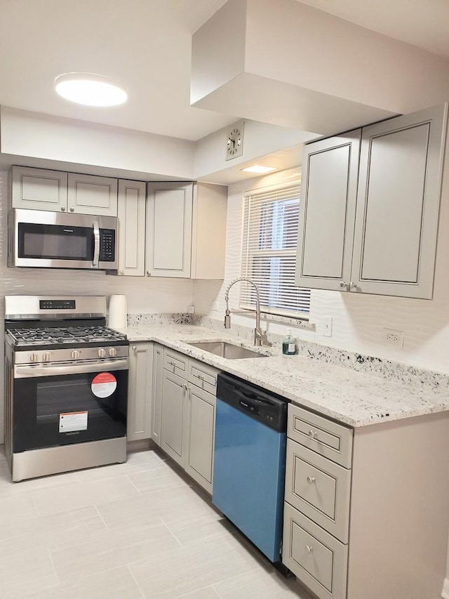 kitchen with stainless steel appliances, gray cabinets, sink, and light stone countertops