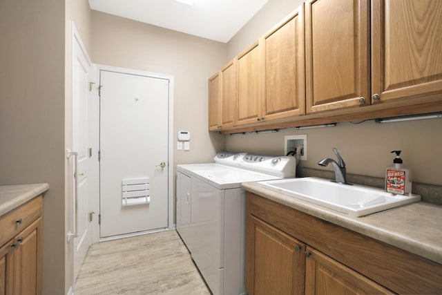 clothes washing area with light hardwood / wood-style flooring, sink, washer and clothes dryer, and cabinets