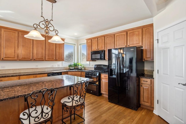 kitchen with hanging light fixtures, black appliances, brown cabinets, and dark stone countertops