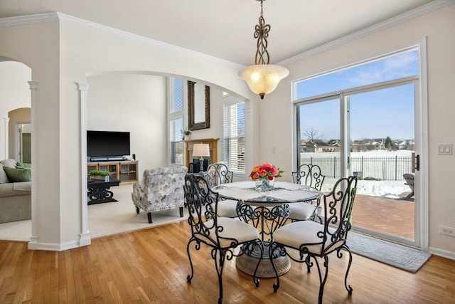 dining room with arched walkways, ornamental molding, and light wood-style floors