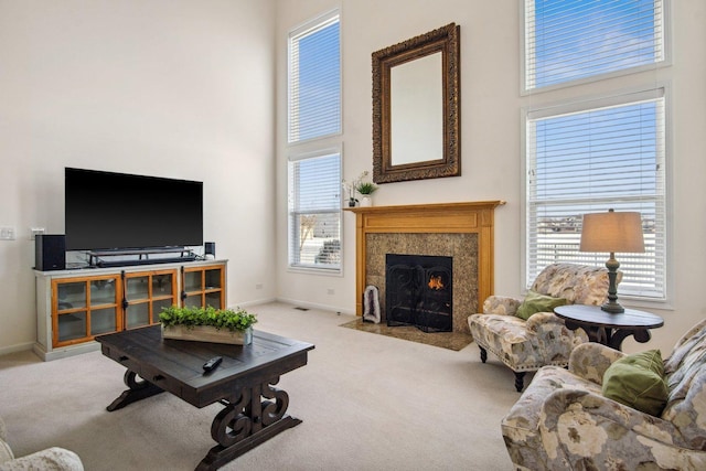 living room with a towering ceiling, a fireplace with flush hearth, baseboards, and light colored carpet