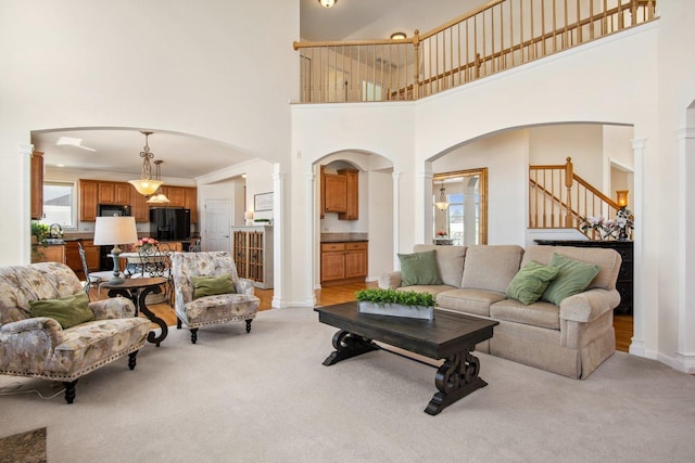 living room featuring arched walkways, light carpet, a high ceiling, stairs, and decorative columns