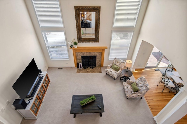 living area featuring arched walkways, wood finished floors, a fireplace with flush hearth, a towering ceiling, and baseboards