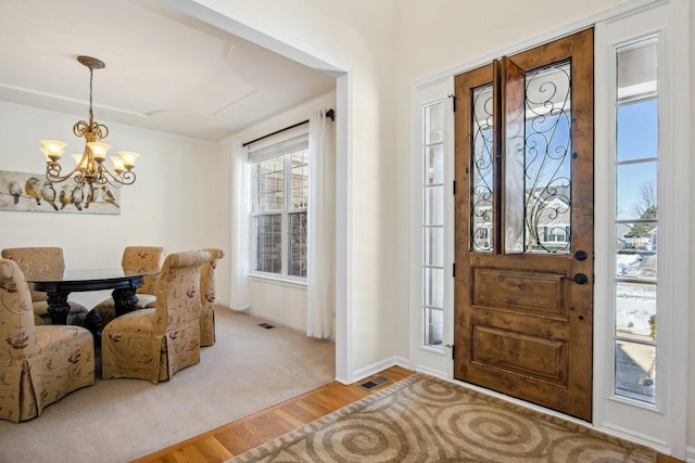 foyer entrance with visible vents, an inviting chandelier, ornamental molding, wood finished floors, and baseboards