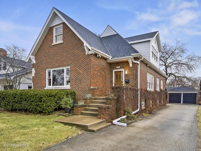 view of front facade with brick siding, a detached garage, roof with shingles, a front yard, and an outdoor structure