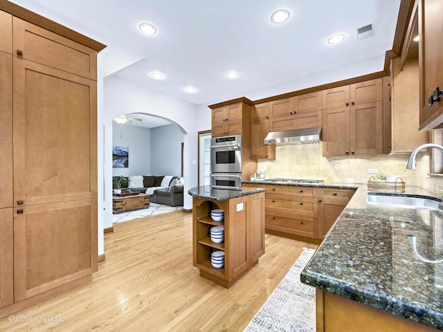 kitchen with arched walkways, stainless steel appliances, a sink, visible vents, and wall chimney exhaust hood