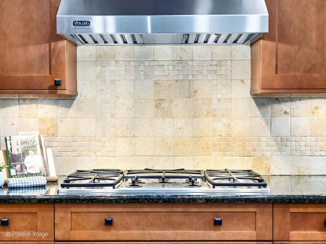 kitchen featuring stainless steel gas cooktop, decorative backsplash, brown cabinetry, dark stone countertops, and exhaust hood