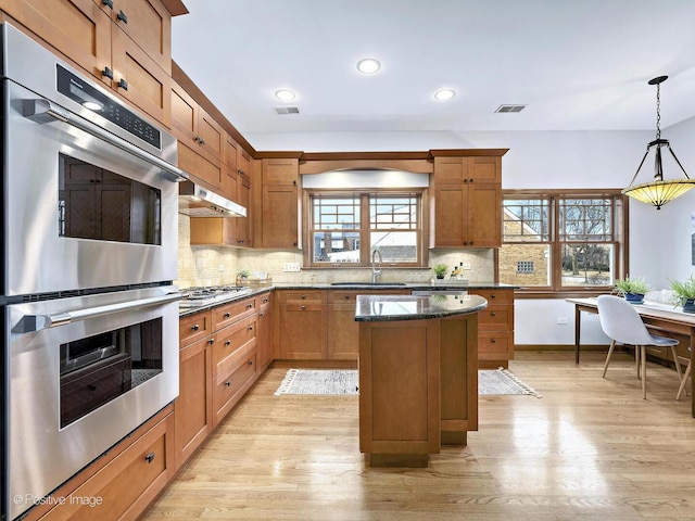 kitchen featuring light wood finished floors, a kitchen island, a sink, stainless steel appliances, and backsplash