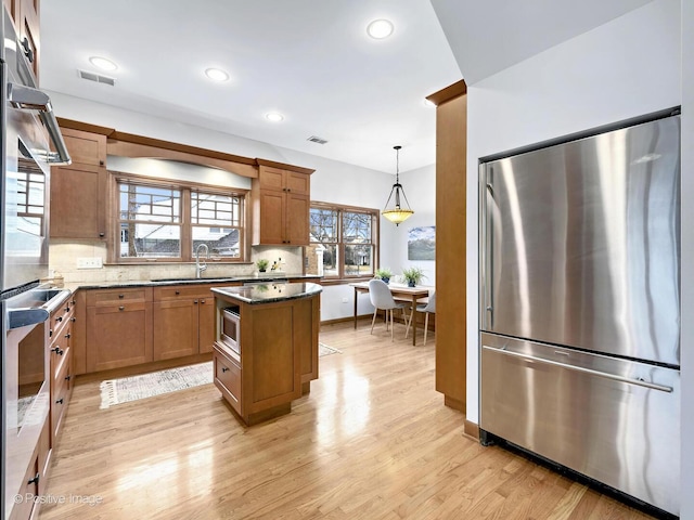 kitchen featuring visible vents, light wood-style flooring, a sink, stainless steel appliances, and backsplash