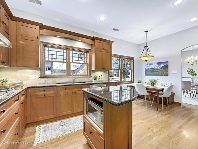 kitchen with visible vents, dark stone counters, stainless steel appliances, light wood-style floors, and a sink