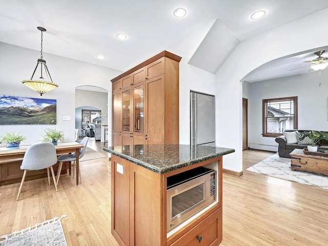 kitchen with arched walkways, stainless steel appliances, a baseboard radiator, light wood-style floors, and dark stone counters