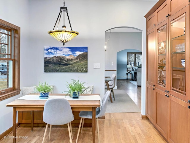 dining room featuring a baseboard heating unit, arched walkways, baseboards, and light wood finished floors