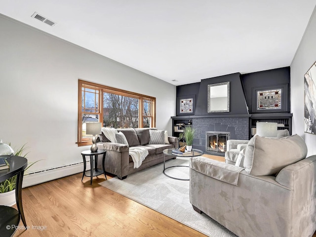 living area featuring a baseboard heating unit, a fireplace, visible vents, and light wood-style floors