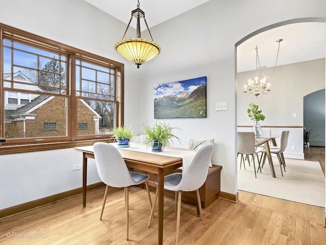 dining room featuring arched walkways, baseboards, a chandelier, and light wood-style floors