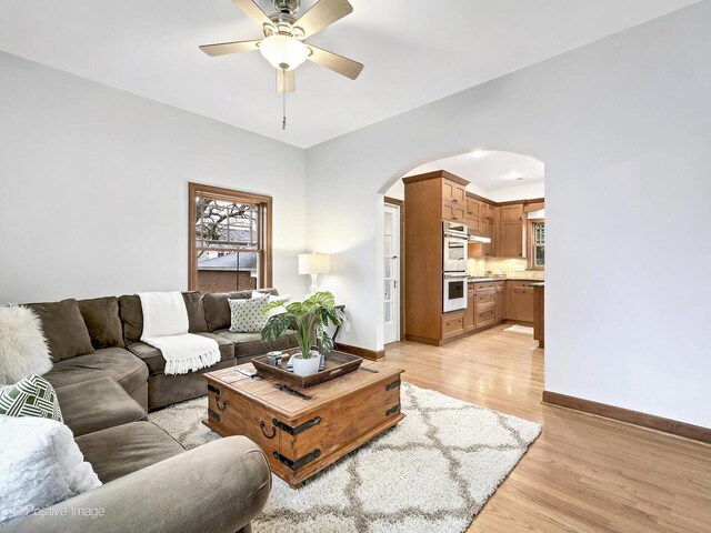 living area with light wood finished floors, baseboards, arched walkways, and a ceiling fan