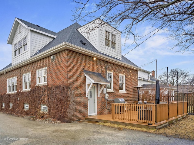 view of front of home with brick siding, roof with shingles, and a wooden deck