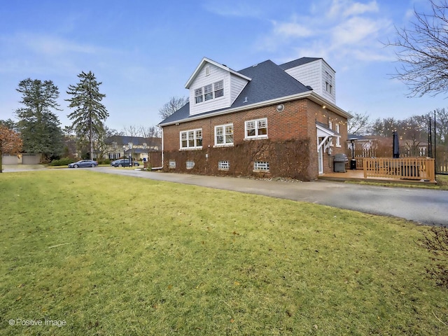 view of side of home featuring a deck, brick siding, a lawn, and aphalt driveway