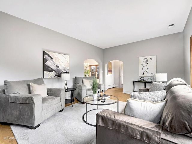 living area featuring arched walkways, light wood-style flooring, a baseboard heating unit, visible vents, and baseboards