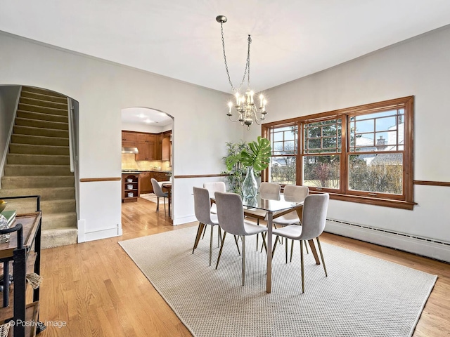 dining area featuring arched walkways, a notable chandelier, light wood-style flooring, stairway, and a baseboard heating unit