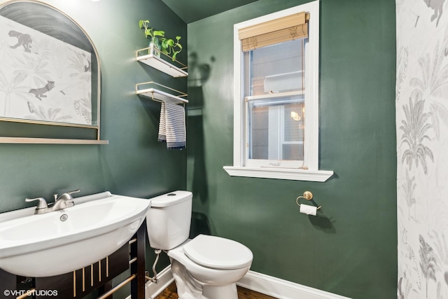 half bathroom with toilet, baseboards, and a sink