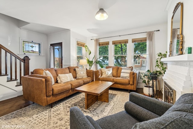 living room with stairway, a brick fireplace, wood finished floors, and crown molding