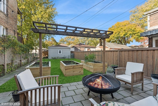 view of patio / terrace featuring an outbuilding, an outdoor fire pit, a fenced backyard, and a vegetable garden