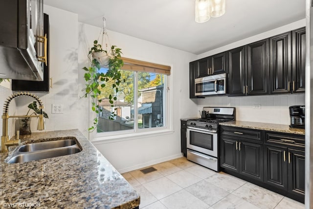 kitchen with dark cabinetry, appliances with stainless steel finishes, backsplash, and a sink