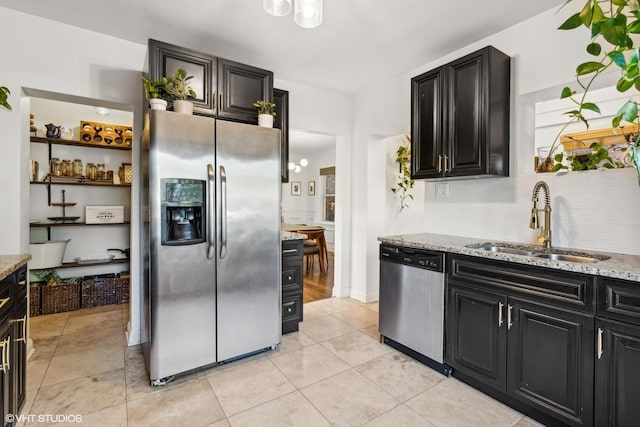 kitchen with a sink, light stone counters, stainless steel appliances, and dark cabinets