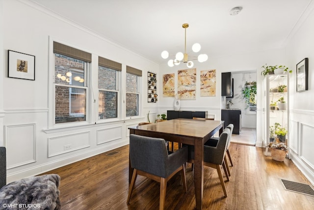 dining area featuring ornamental molding, wood finished floors, visible vents, and a decorative wall