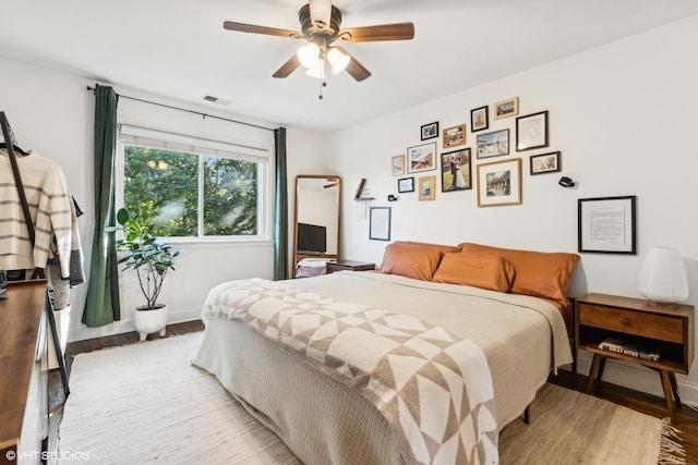 bedroom with a ceiling fan, wood finished floors, visible vents, and baseboards