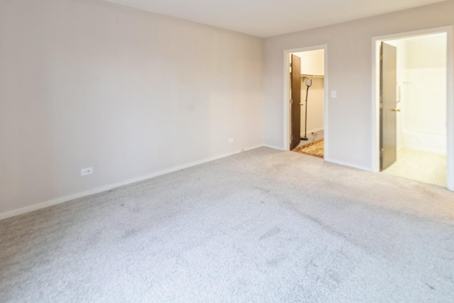 unfurnished bedroom with a walk in closet, light colored carpet, and ensuite bath