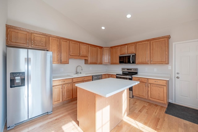 kitchen with vaulted ceiling, appliances with stainless steel finishes, sink, a center island, and light hardwood / wood-style flooring