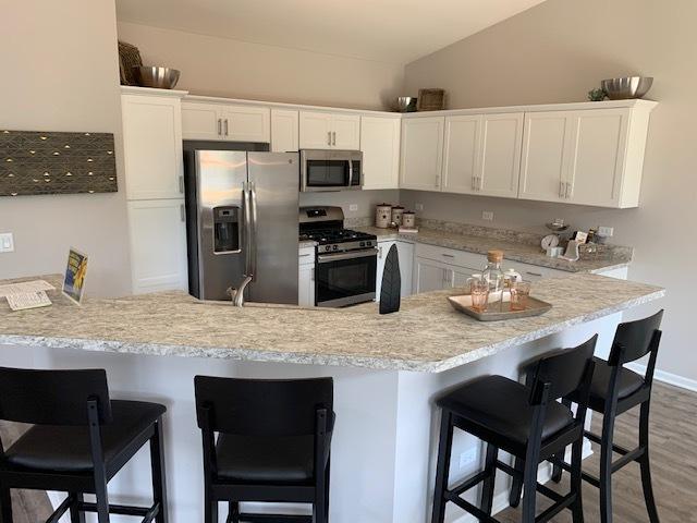 488 Ridge Ln, Bolingbrook, IL 60440 - kitchen featuring white cabinetry, lofted ceiling, a kitchen bar, kitchen peninsula, and stainless steel appliances