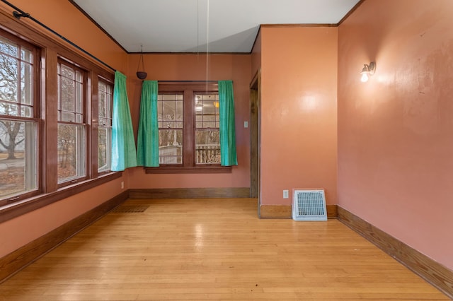 unfurnished room featuring a healthy amount of sunlight, visible vents, baseboards, and wood finished floors