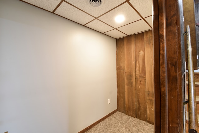 interior space featuring a paneled ceiling, visible vents, wooden walls, and baseboards