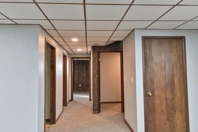 hall featuring a paneled ceiling, light colored carpet, and baseboards