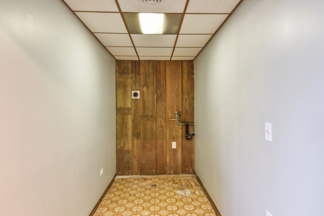 hall featuring a paneled ceiling, wooden walls, and light floors